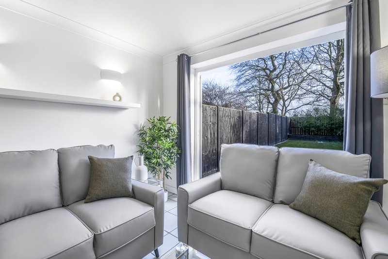 Modern living room with grey sofas, cushions, potted plant and garden view through patio doors