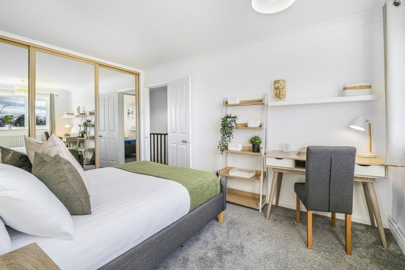 Modern bedroom with double bed, wooden shelving, desk chair, and mirrored wardrobe doors