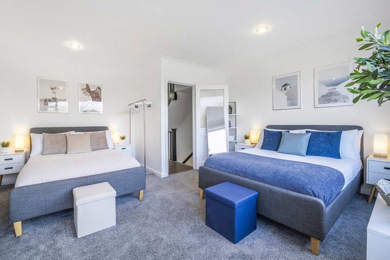 Bright shared bedroom with two double beds, blue bedding, wooden legs, and modern furnishings