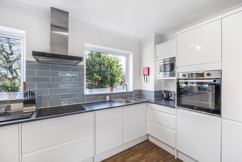Modern white kitchen with dark tile backsplash, black countertops, stainless steel appliances and garden view