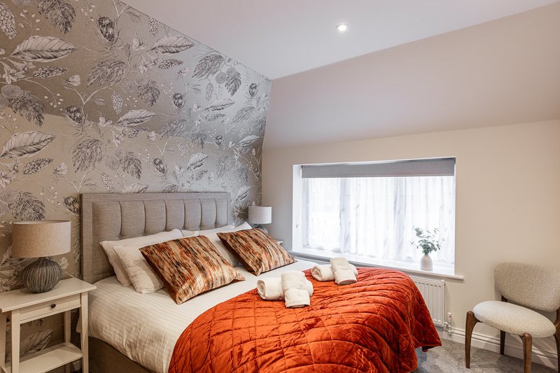 Bright bedroom with double bed, patterned headboard wall, orange bedding and matching pillows