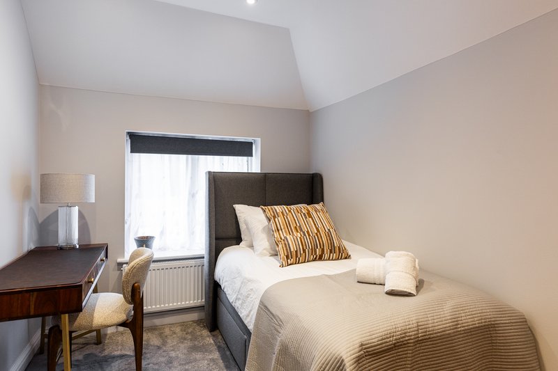 Bedroom with single bed, dark headboard, wooden desk, lamp and window with blind
