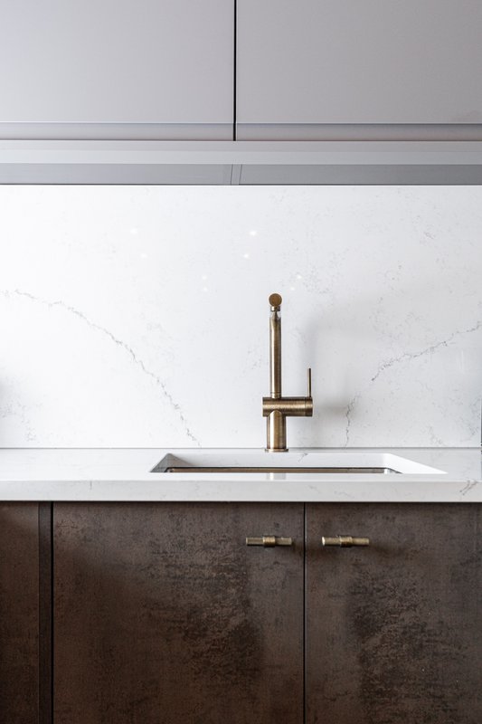Modern kitchen sink with brass tap, white marble backsplash and dark cabinetry