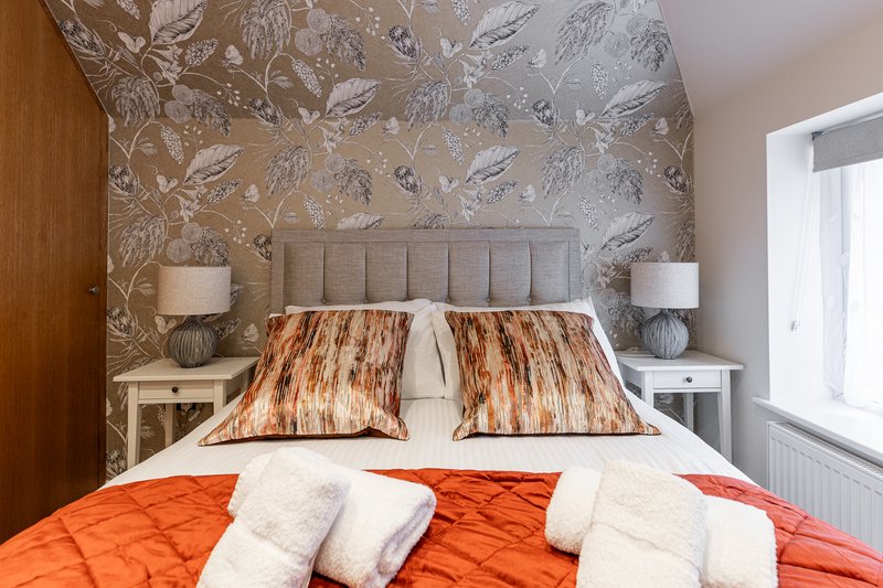 Bedroom with double bed, patterned headboard, orange bedding and white pillows