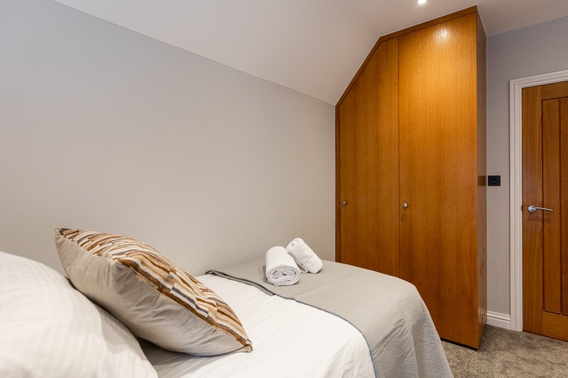 Bedroom with single bed, wooden wardrobe, white bedding and rolled towels