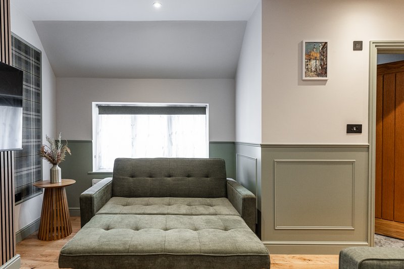Modern bedroom with olive green upholstered bed, wooden floor, and window with natural light