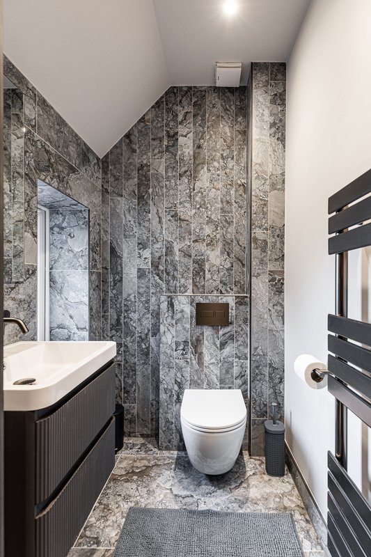 Modern bathroom with marble-effect tiling, white toilet, black vanity unit and heated towel rail