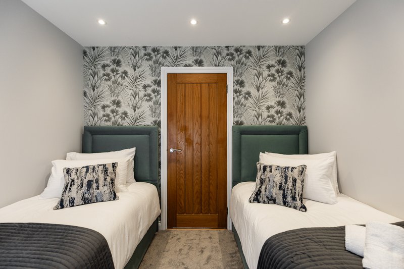 Twin bedroom with two single beds, botanical wallpaper, wooden door and recessed ceiling lights