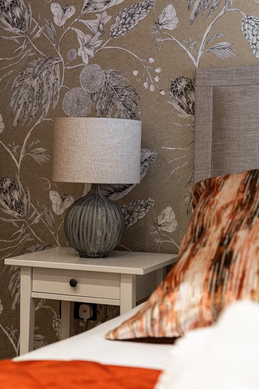 Bedroom bedside table with lamp, drawer, and patterned wallpaper backdrop