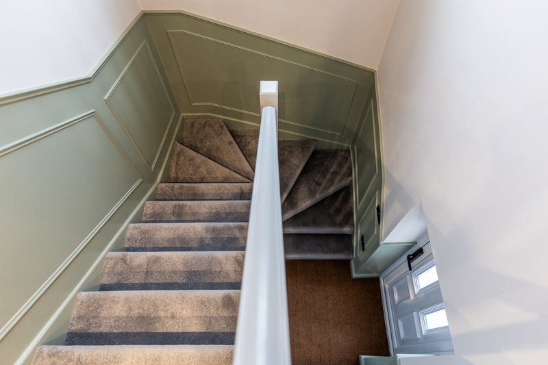 Staircase with brown carpet and white handrail viewed from above, showing landing below