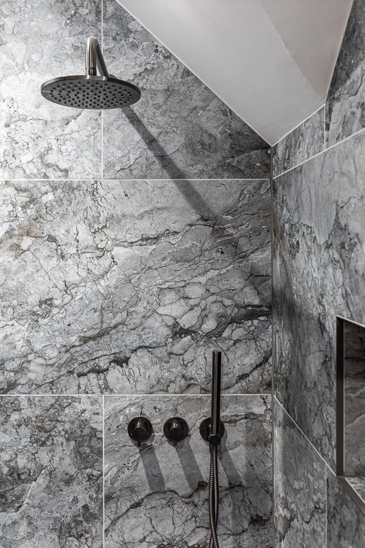 Modern bathroom shower with marble-look tile walls, black fixtures and overhead showerhead