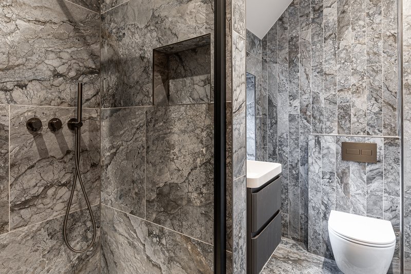 Modern bathroom with marble tile walls, walk-in shower, toilet and vanity