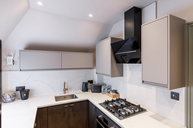 Modern kitchen with white countertops, gas cooktop, black range hood and wooden cabinetry