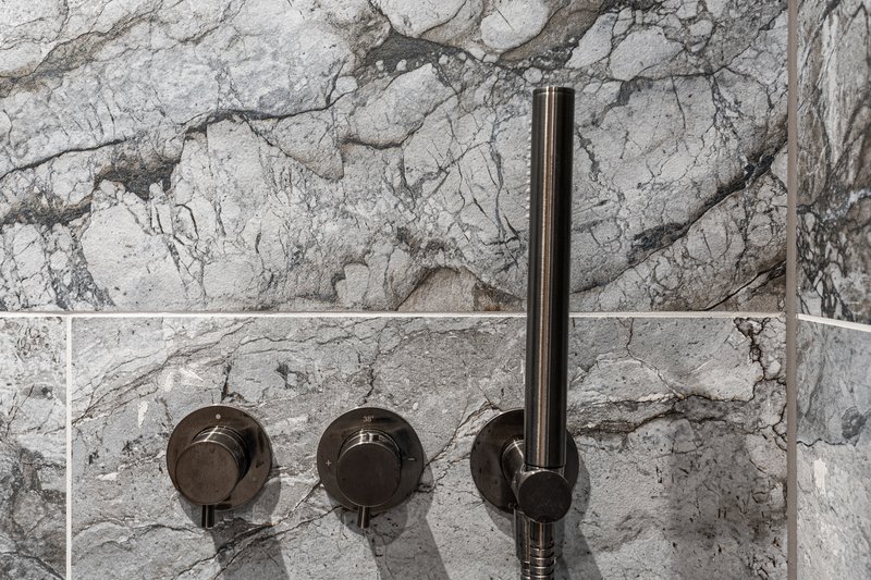 Bathroom shower wall with marble tile and dark metal fixtures and handles