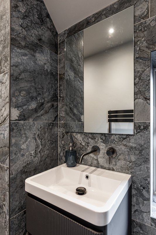 Modern bathroom with dark marble tiles, white basin, mirror and black fixtures