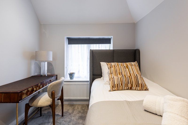 Bright bedroom with single bed, dark headboard, wooden desk, chair and table lamp