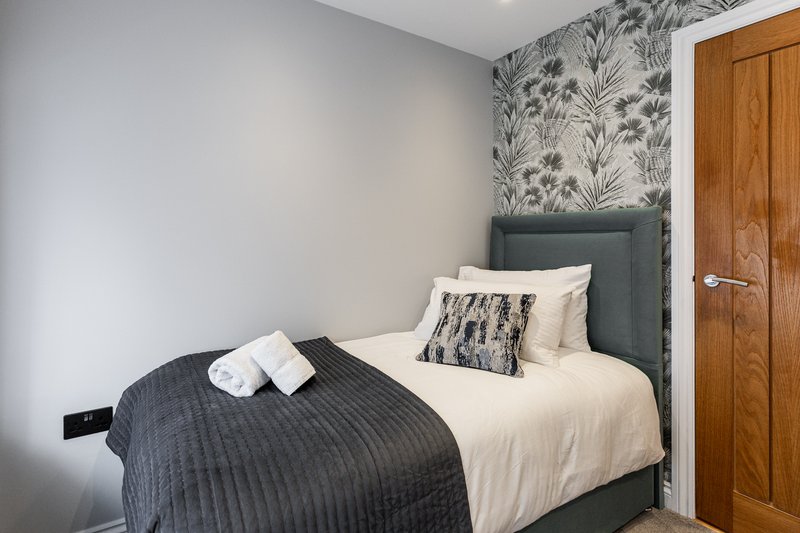 Bedroom with double bed, grey headboard, patterned wallpaper, and wooden door