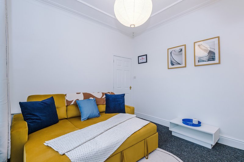 Bright bedroom with yellow sofa, blue and yellow cushions, white bedding, and framed wall art