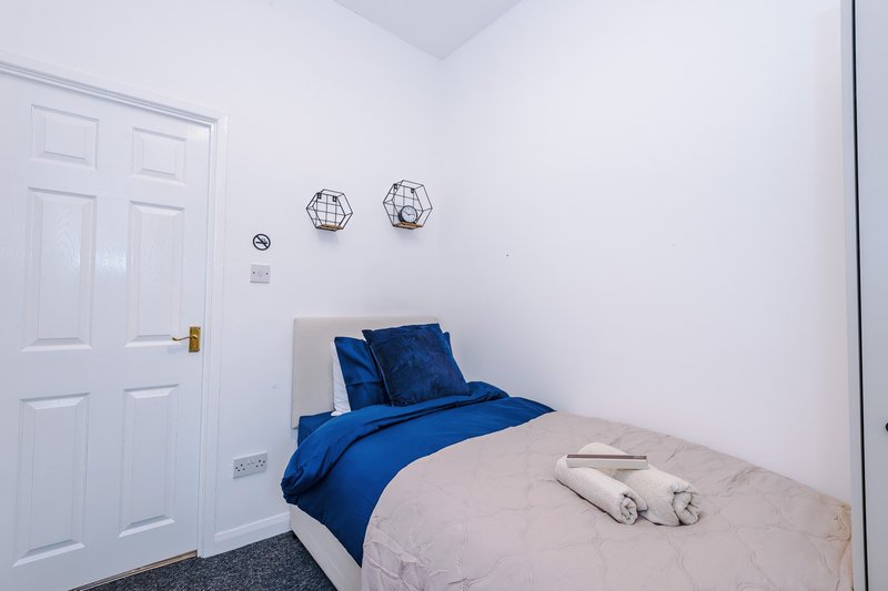 Compact bedroom with single bed, blue bedding, white wardrobe and wall decorations
