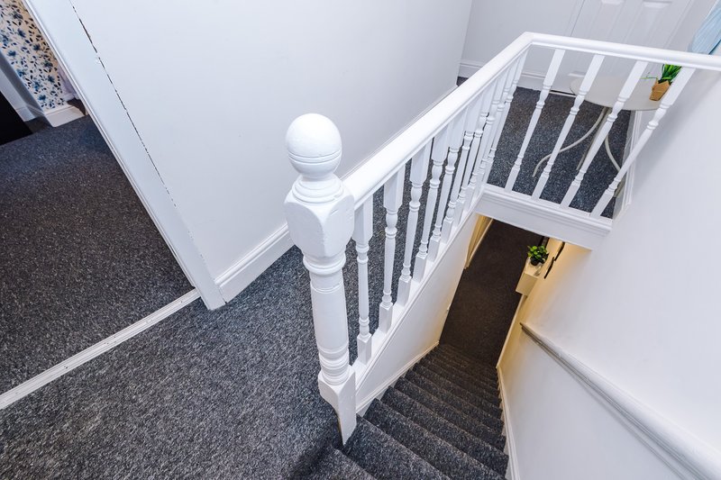 Staircase with white bannister and black carpet treads descending into hallway