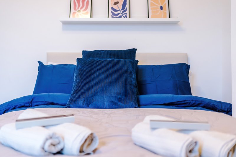 Bedroom with blue cushions and pillows on bed, white headboard, framed wall art above