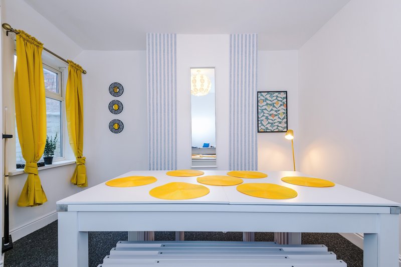 Modern dining room with white table, yellow place mats, bright window with yellow curtains