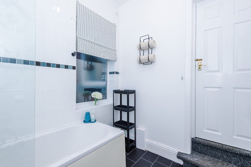 Modern bathroom with white bathtub, blue tile accents, black shelving unit, and white door