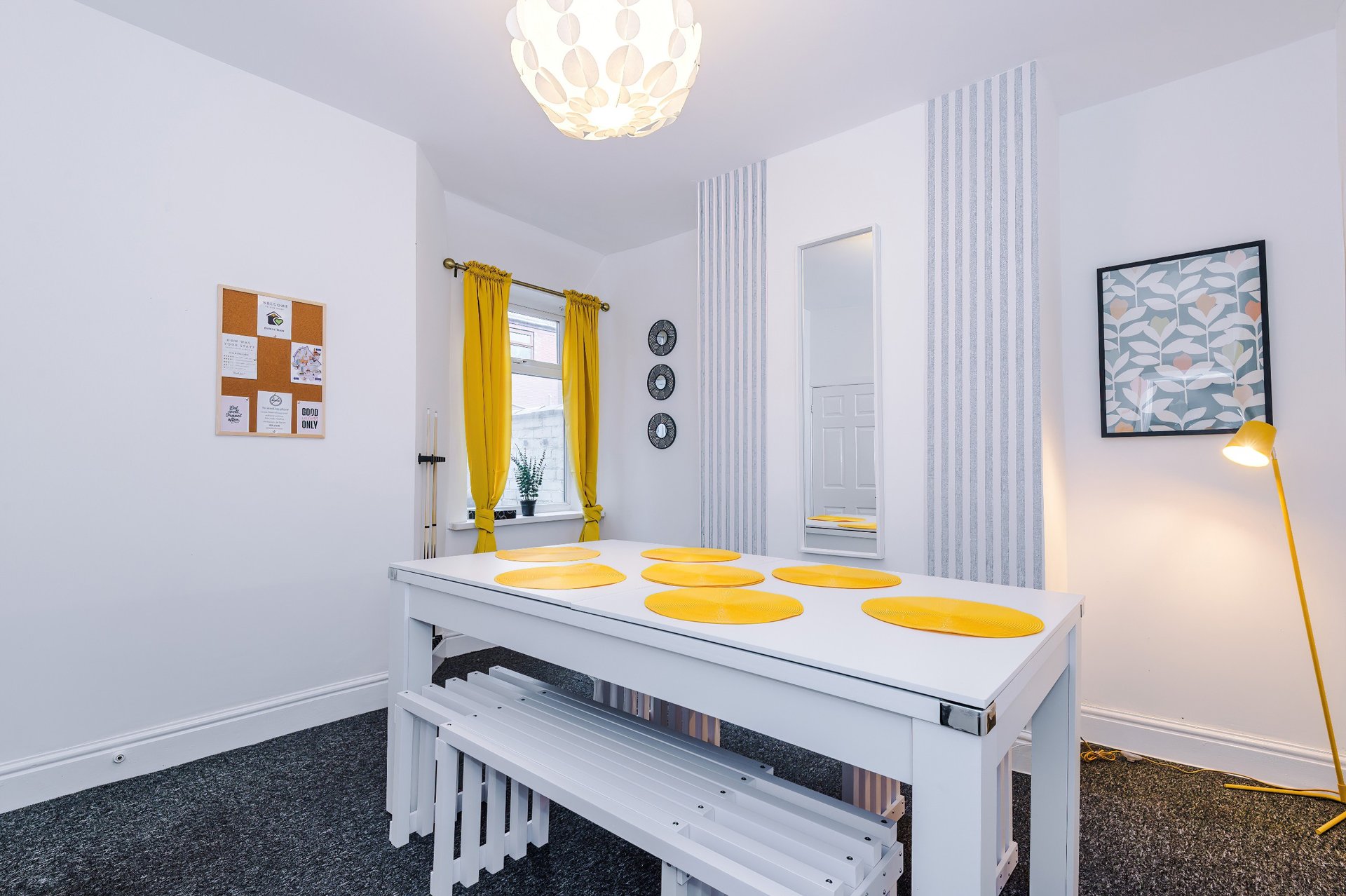 Modern kitchen with white dining table, yellow accents, pendant light and framed wall art