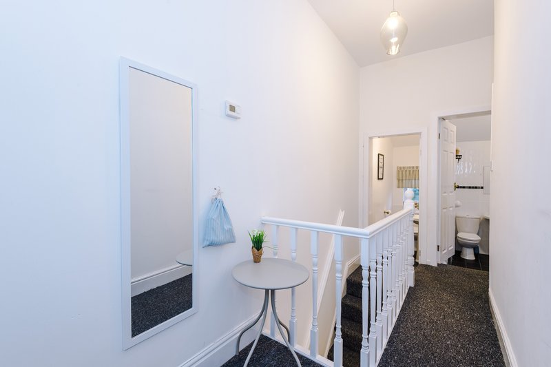 Hallway with white walls, small round table, baby gate, and doorways leading to other rooms
