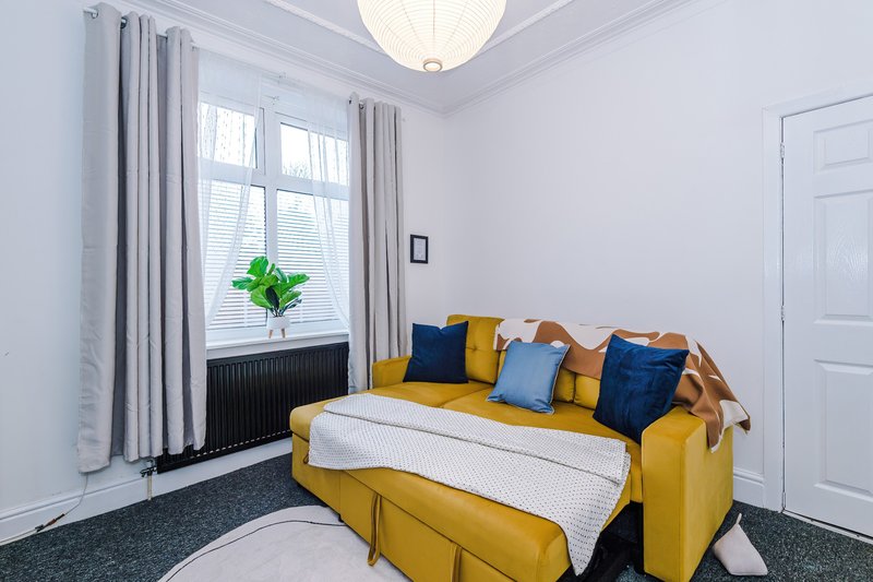 Bright bedroom with yellow sofa, colorful cushions, large window and ceiling light