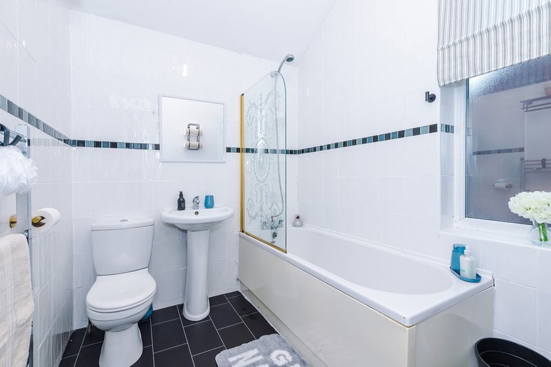 Clean bathroom with toilet, pedestal sink, bathtub, shower enclosure and black floor tiles