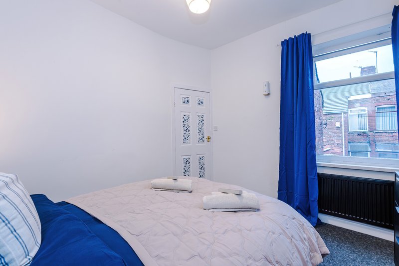Bright bedroom with double bed, blue bedding, white wardrobe and blue curtains