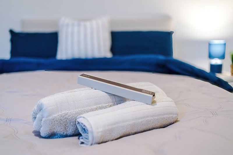 Bedroom with rolled white towels on bed, blue sofa and striped pillows behind