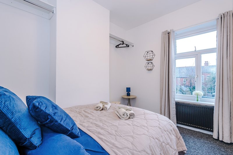 Bright modern bedroom with double bed, blue cushions, large window overlooking city