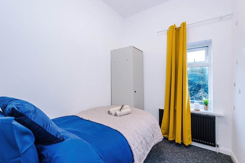 Bright bedroom with blue duvet, single bed, yellow curtains and window view