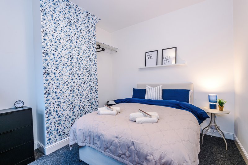 Modern bedroom with double bed, blue bedding, patterned accent wall and white walls