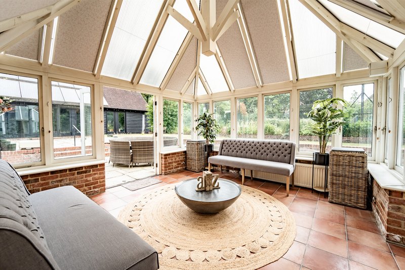 Bright conservatory with skylights, seating area, round rug, potted plants and garden views
