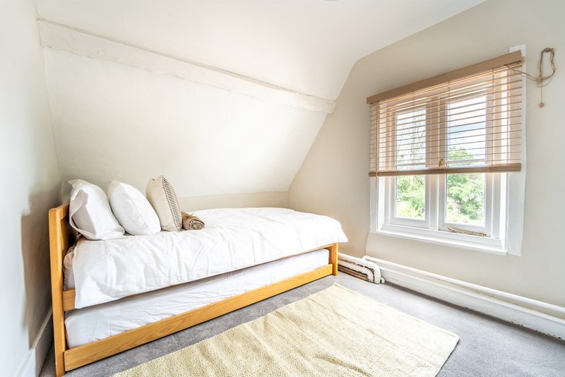 Bright attic bedroom with wooden bed, white bedding, and slatted window blinds