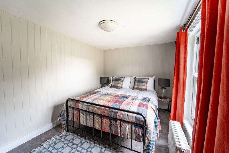 Bedroom with metal-frame bed, checkered bedding, red curtains and wooden wall paneling