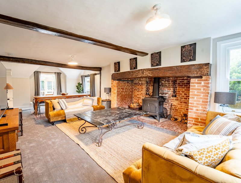 Spacious living room with brick fireplace, exposed beams, orange upholstered seating and windows