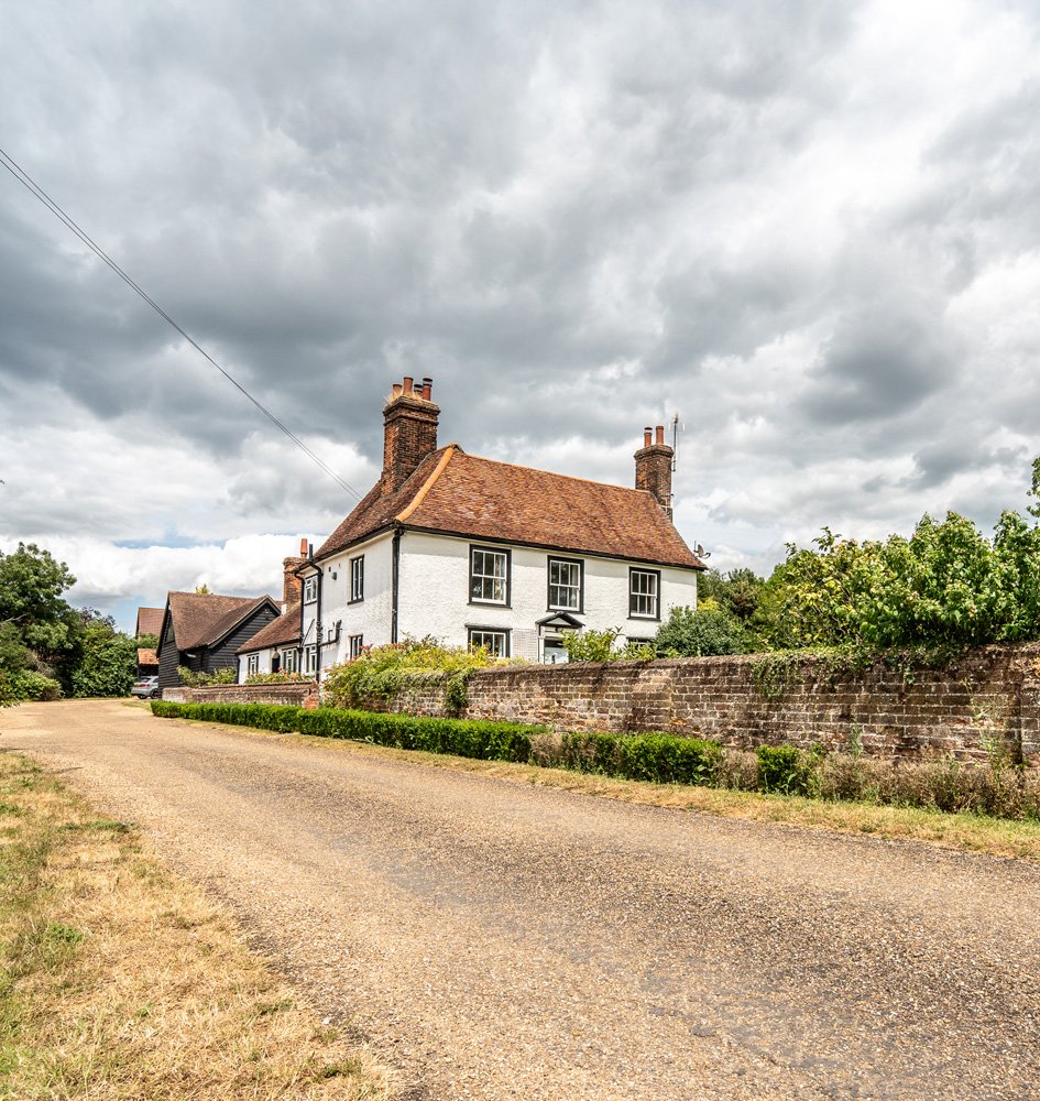Traditional white cottage with red-tiled roof, stone boundary wall, and gravel driveway approach