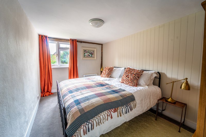 Bright bedroom with double bed, patterned duvet, orange curtains and wooden wall panelling