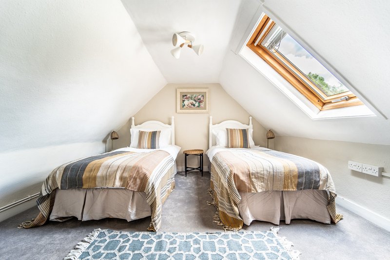 Attic bedroom with two single beds, striped bedding, skylight window and patterned rug