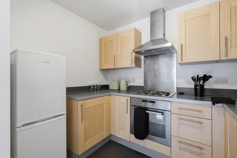 Modern kitchen with light wood cabinets, stainless steel cooker hood, and black countertops