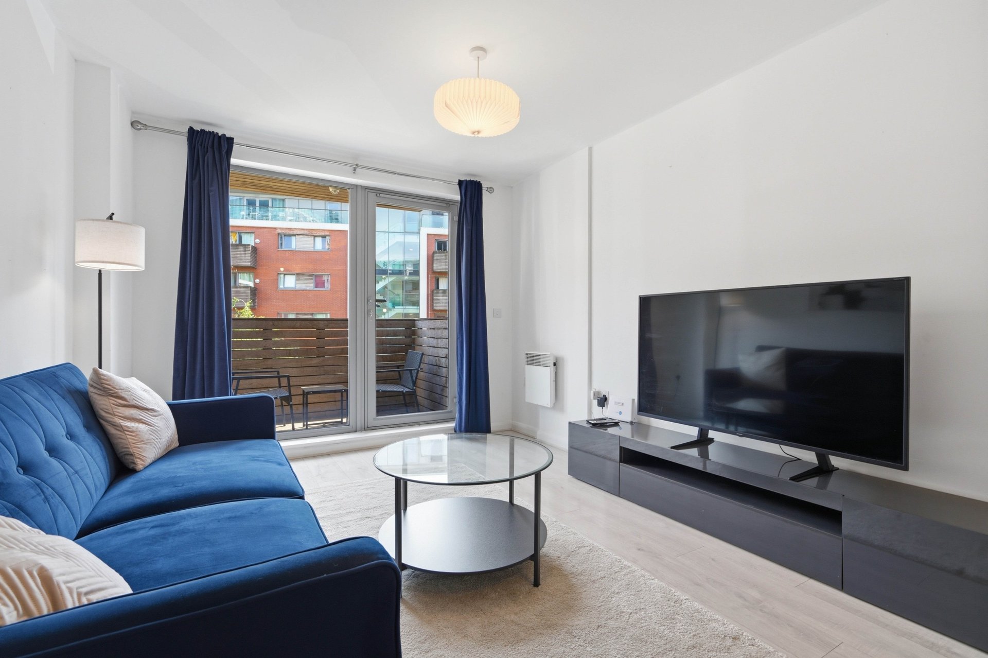 Modern living room with blue sofa, TV, glass coffee table and pendant ceiling light