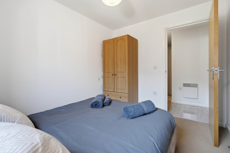 Bedroom with double bed, blue bedding, wooden wardrobe and white walls