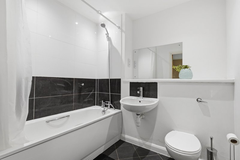Modern bathroom with bathtub, black tile surround, white sink and toilet, mirror