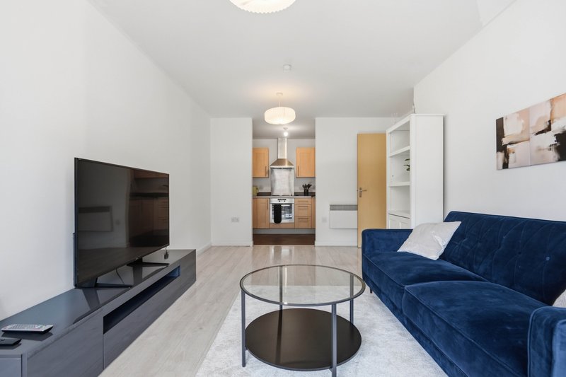 Open-plan living room with navy sofa, TV unit, round glass table and kitchen beyond