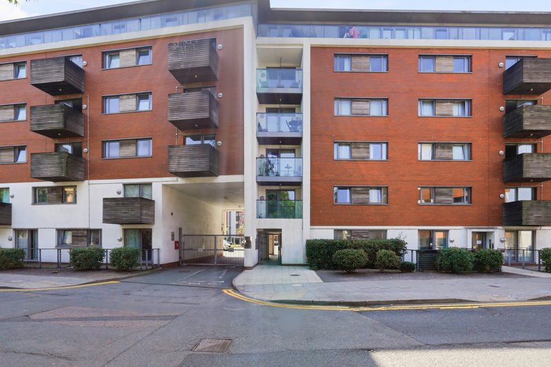 Modern multi-story residential building with brick facade, balconies, and ground-floor entrance
