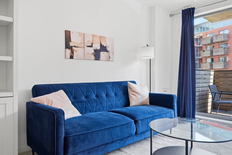 Modern living room with blue velvet sofa, abstract wall art, floor lamp and city view